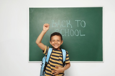 Little African-American child near chalkboard with text BACK TO SCHOOL