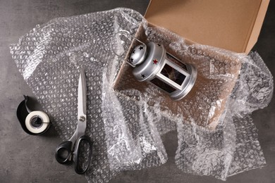 Photo of Beautiful decorative lantern, bubble wrap, scissors and cardboard box on dark grey table, flat lay