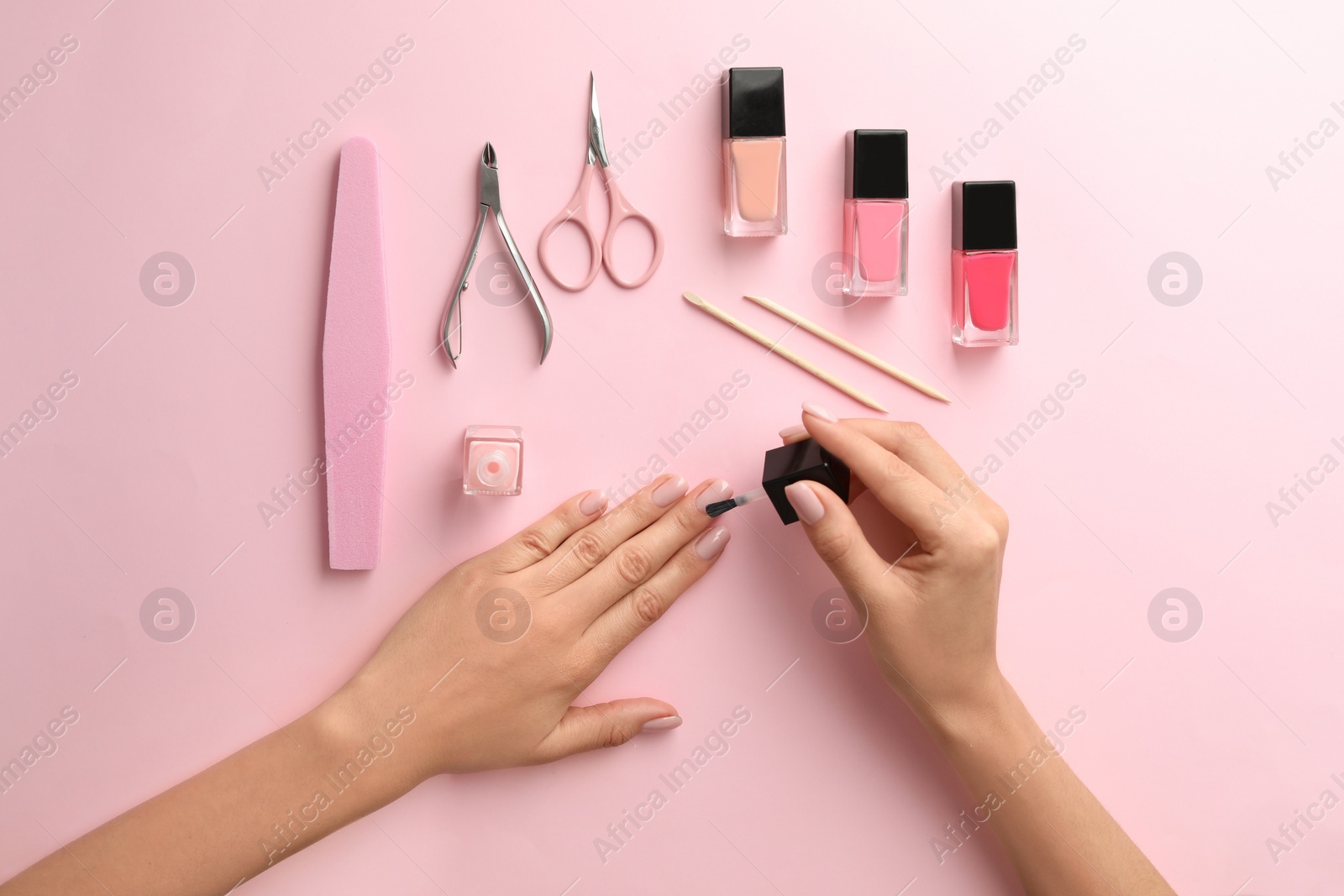 Photo of Woman applying nail polish on color background, top view