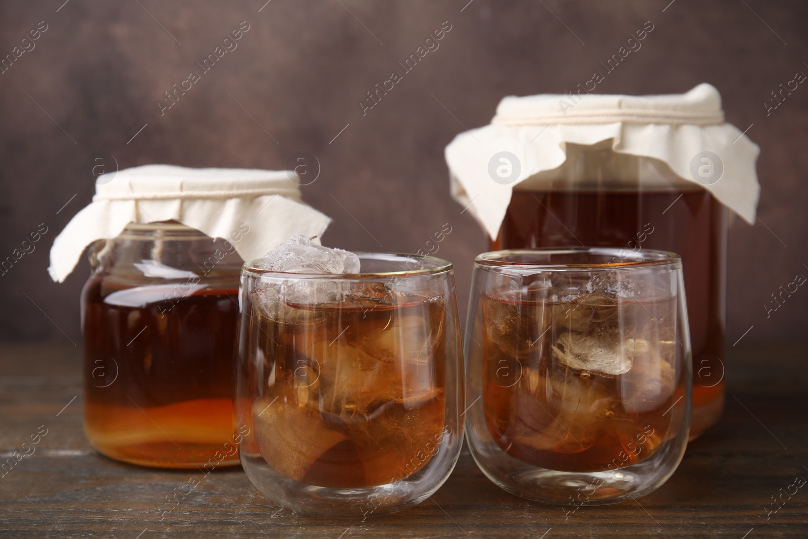 Photo of Tasty kombucha with ice cubes on wooden table, closeup