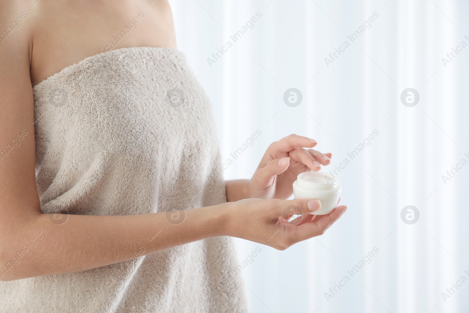 Photo of Young woman holding jar of cream at home, closeup