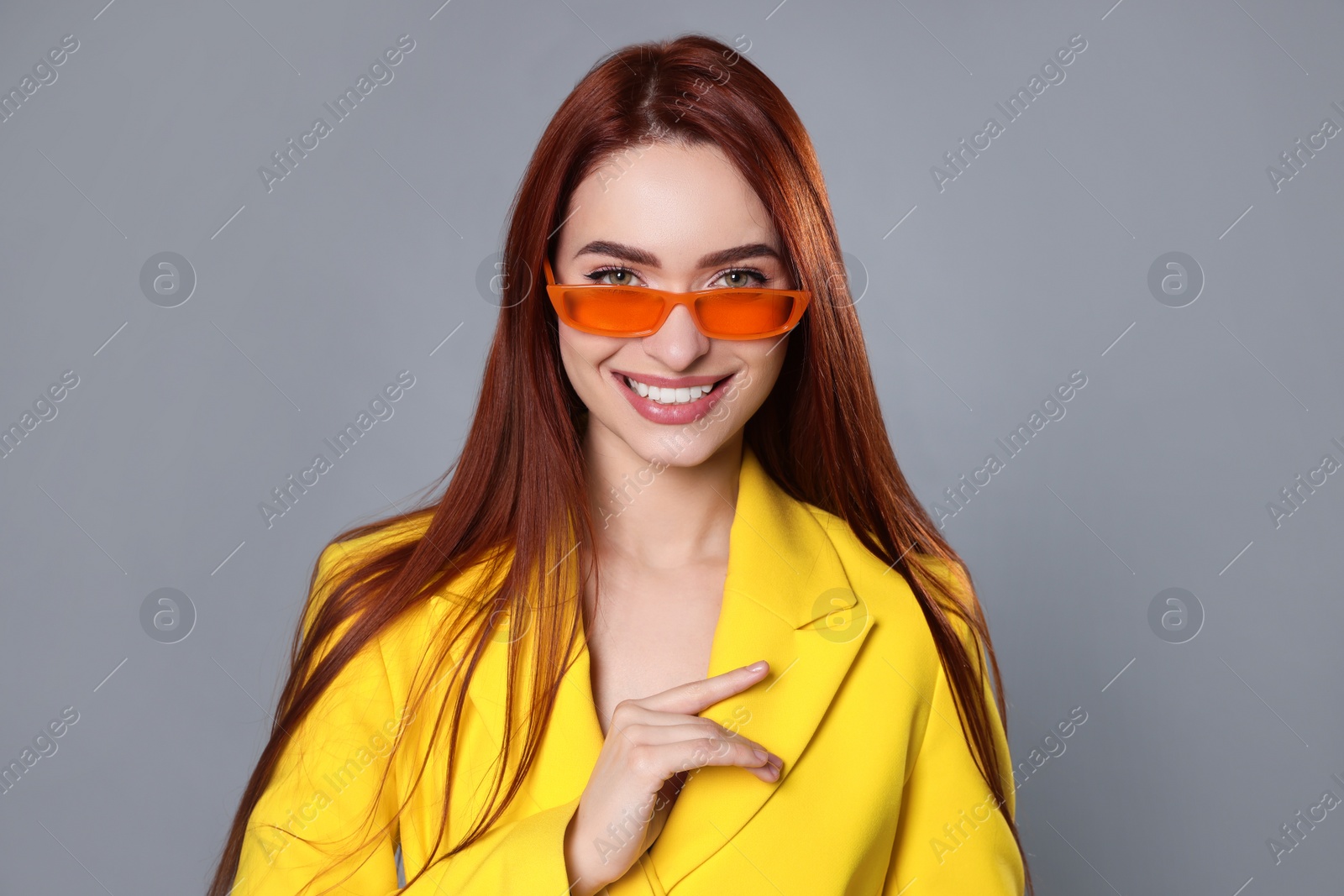 Photo of Stylish woman with red dyed hair and orange sunglasses on light gray background