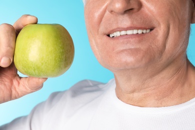 Photo of Mature man with healthy teeth holding apple on color background, closeup