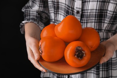 Woman holding delicious ripe juicy persimmons on black background, closeup