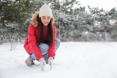 Young woman rolling snowball outdoors on winter day. Space for text