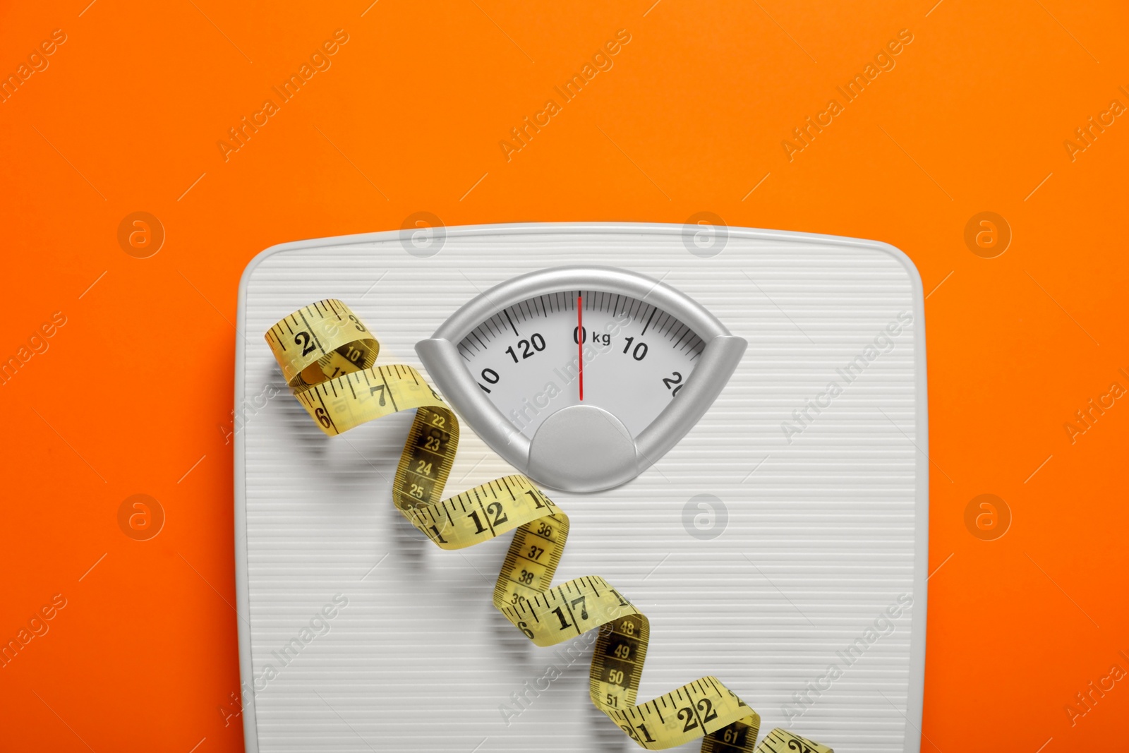 Photo of Bathroom scale and measure tape on orange background, top view