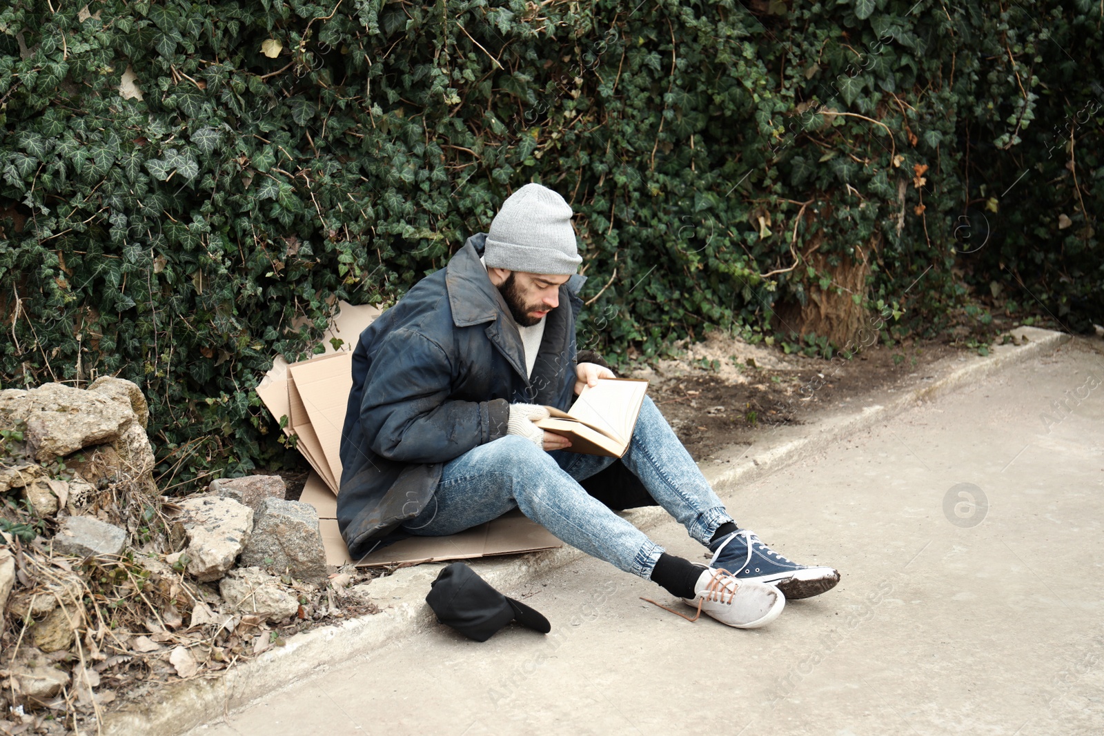 Photo of Poor homeless man with book on street in city