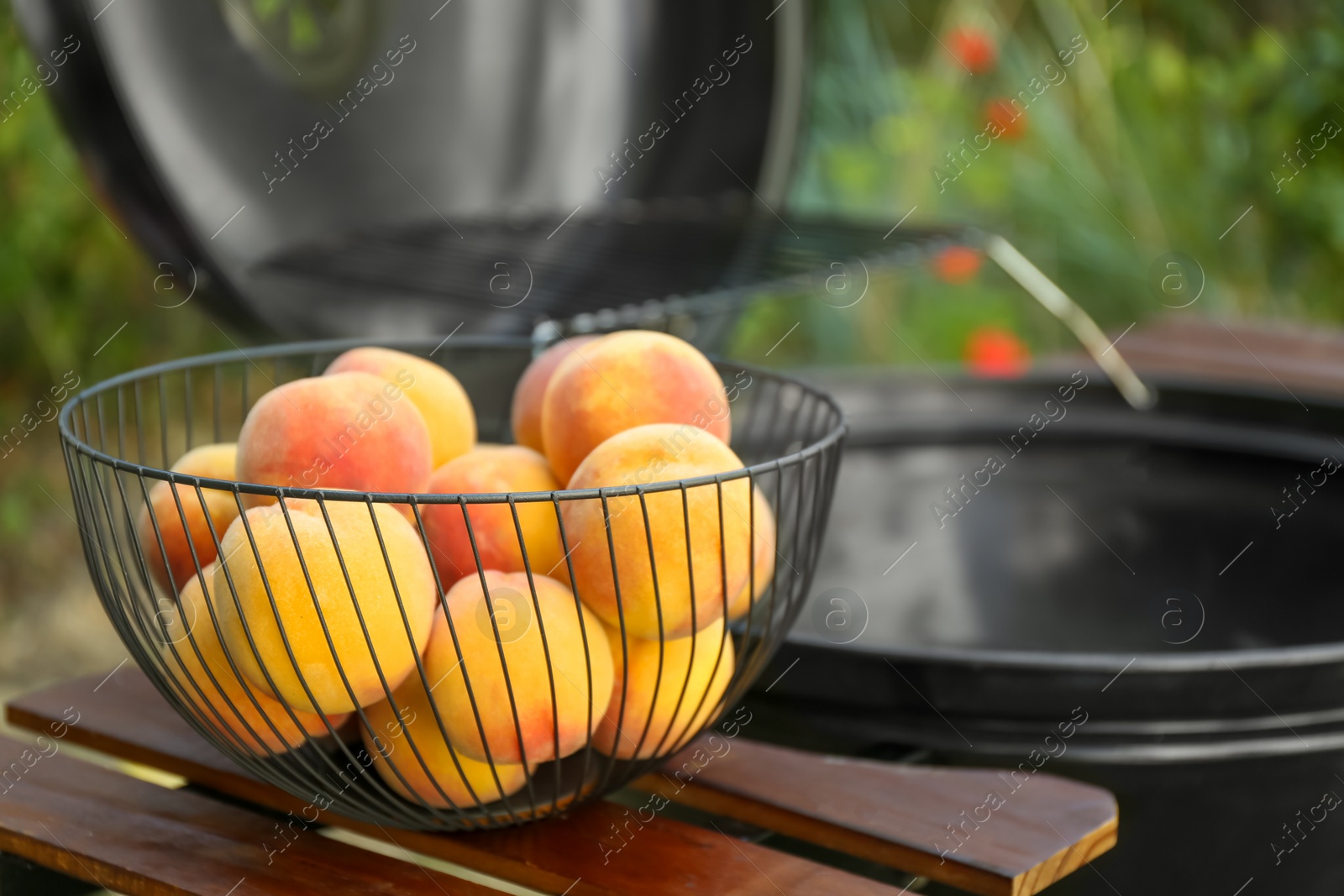 Photo of Fresh peaches on wooden table near modern grill outdoors