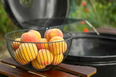 Fresh peaches on wooden table near modern grill outdoors