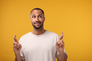 Photo of Young man crossing his fingers on orange background, space for text