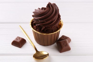 Photo of Delicious cupcake and chocolate pieces on white wooden table, closeup