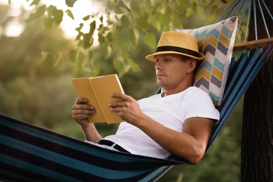 Photo of Man reading book in comfortable hammock at green garden