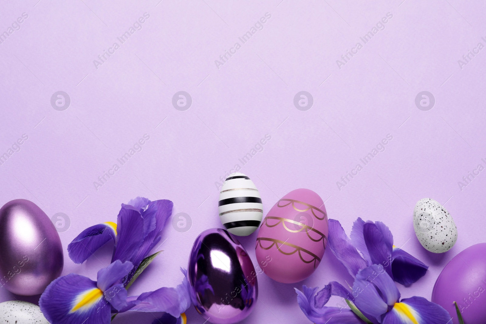 Photo of Flat lay composition with iris flowers and beautifully painted eggs on violet background, space for text. Easter celebration