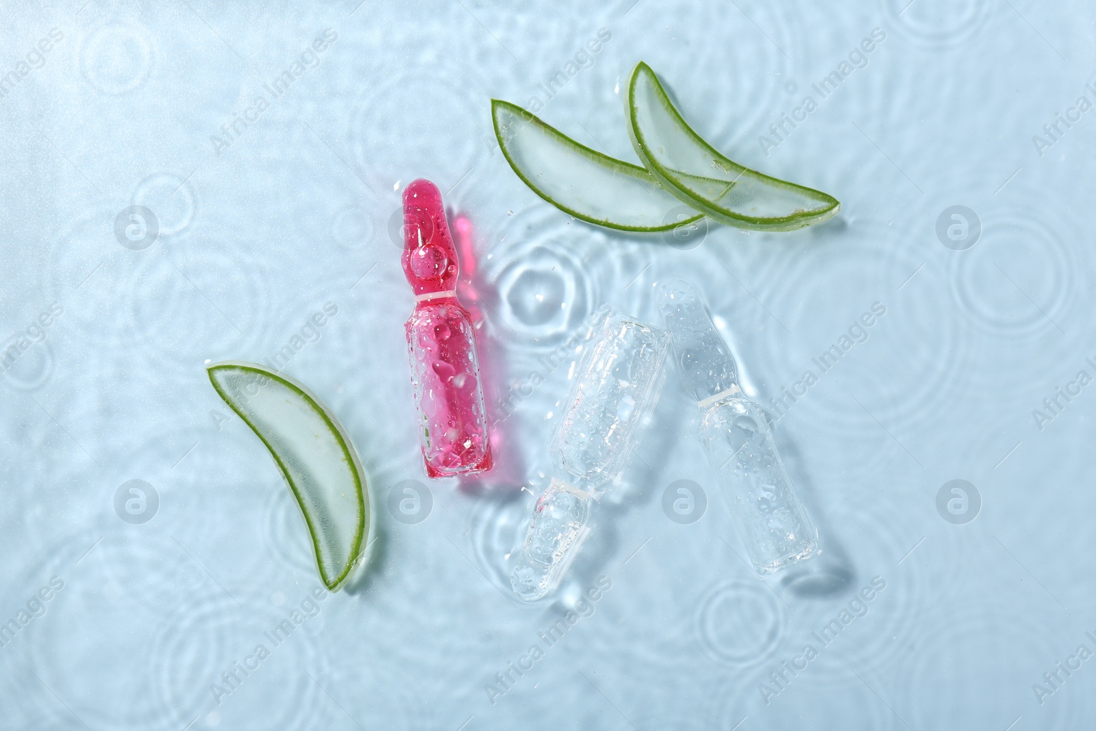 Photo of Skincare ampoules with extract of aloe vera and cut leaves in water on light blue background, flat lay