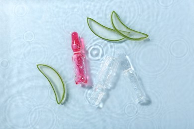 Skincare ampoules with extract of aloe vera and cut leaves in water on light blue background, flat lay