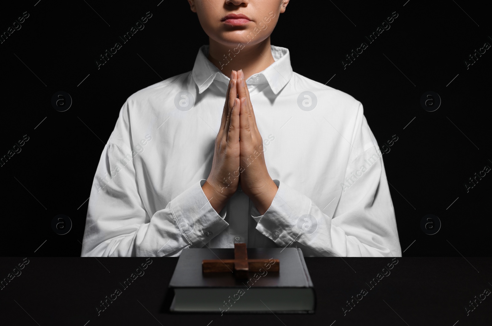Photo of Woman holding hands clasped while praying at table with Bible and cross, closeup