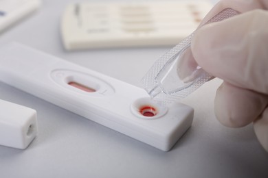 Doctor dropping buffer solution onto disposable express test cassette on light background, closeup