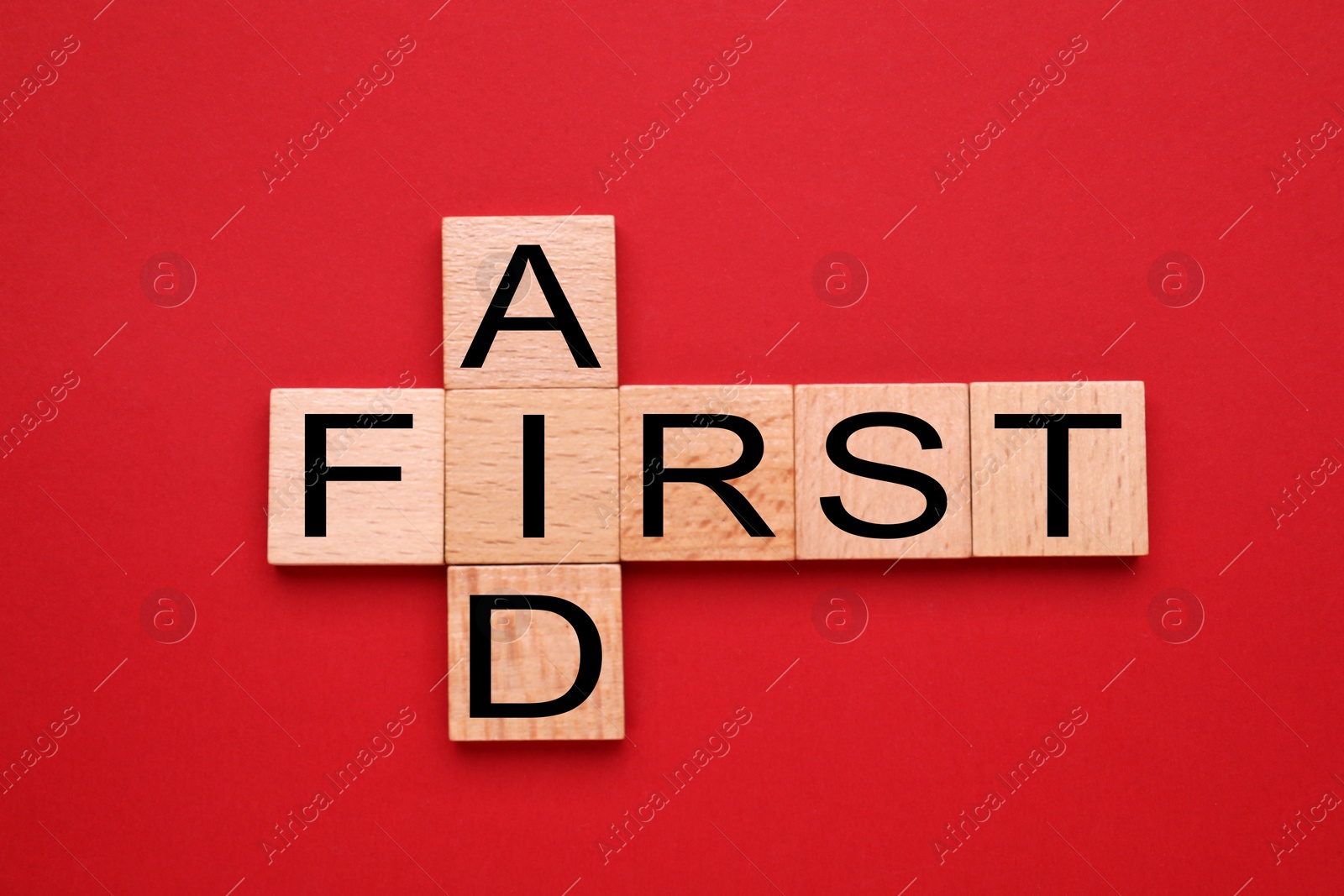 Photo of Words First Aid made of wooden cubes on red background, flat lay