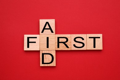 Photo of Words First Aid made of wooden cubes on red background, flat lay