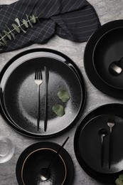 Photo of Stylish table setting. Dishes, cutlery and eucalyptus branch on grey surface, flat lay