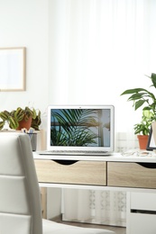 Photo of Houseplants and laptop on table in office interior