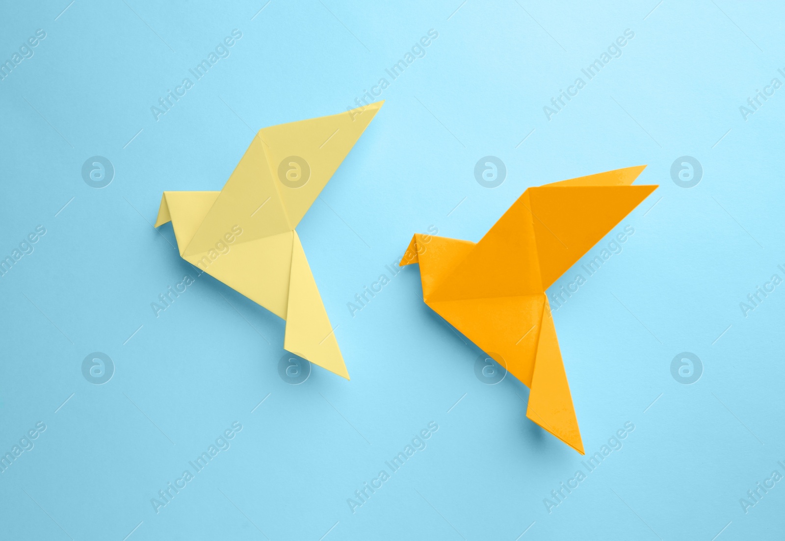Photo of Origami art. Colorful handmade paper birds on light blue background, flat lay