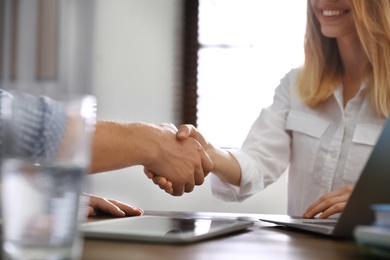 Business partners shaking hands at table after meeting in office, closeup