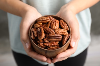Photo of Woman holding bowl with shelled pecan nuts in hands, closeup