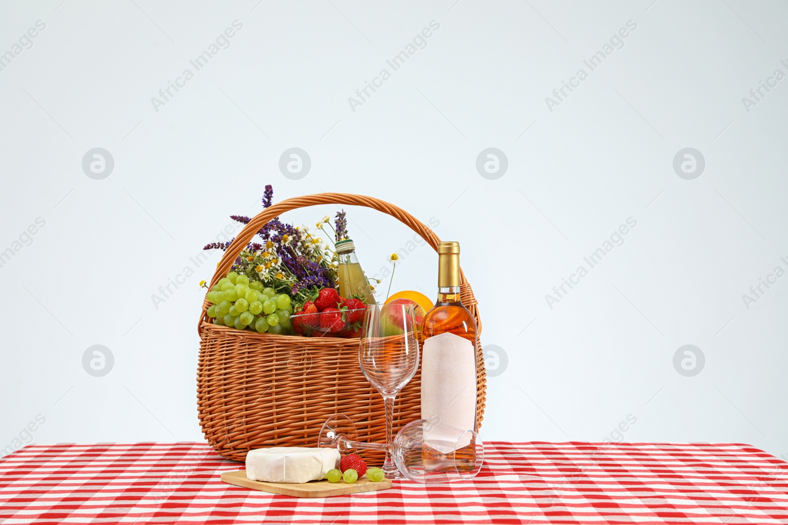 Photo of Picnic basket with wine and products on checkered tablecloth against white background