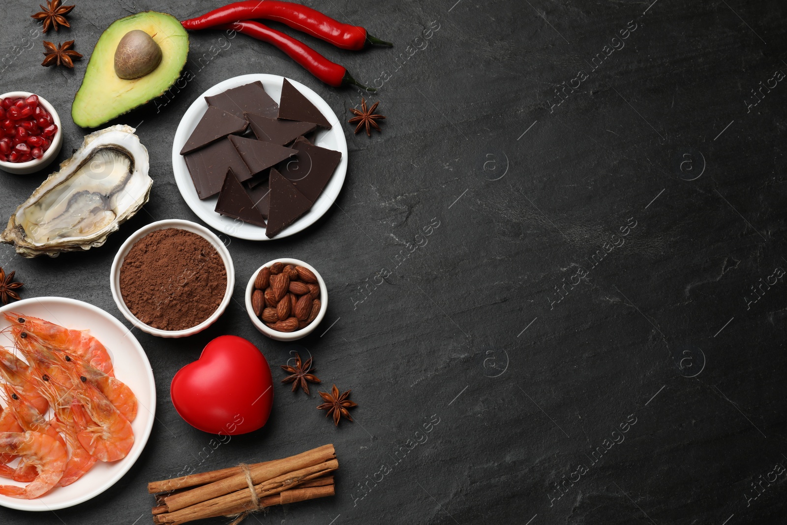 Photo of Natural aphrodisiac. Different food products and heart model on black table, flat lay. Space for text