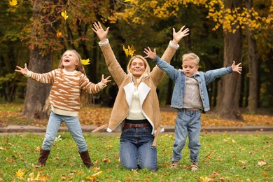 Photo of Happy mother and her children playing with dry leaves in autumn park