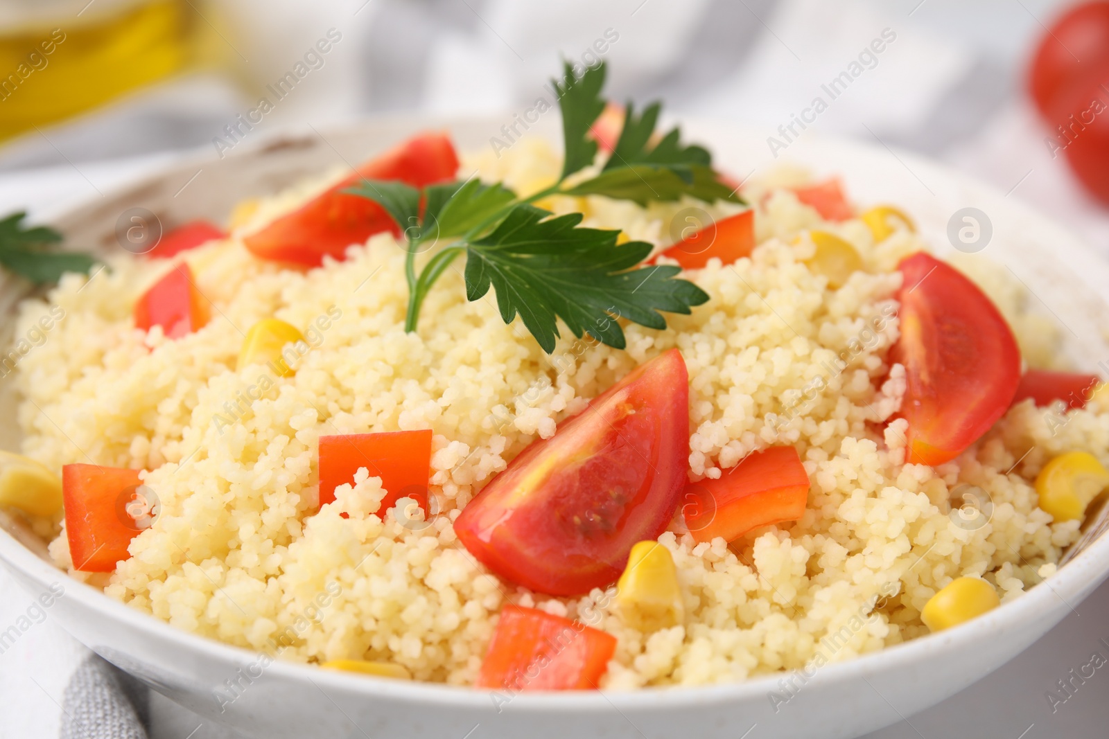 Photo of Tasty couscous with parsley, corn and tomatoes in bowl on table, closeup