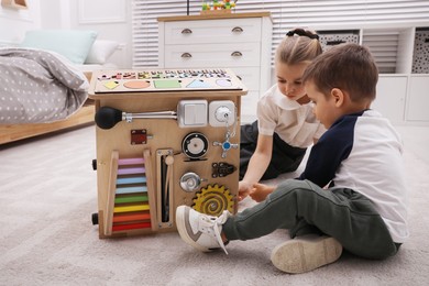 Photo of Little boy and girl playing with busy board house on floor in room