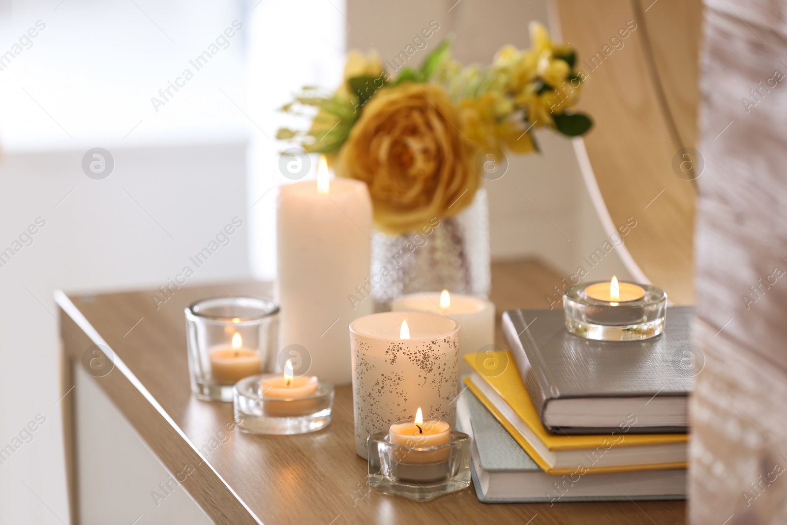 Photo of Beautiful burning candles, books and flowers on table at home