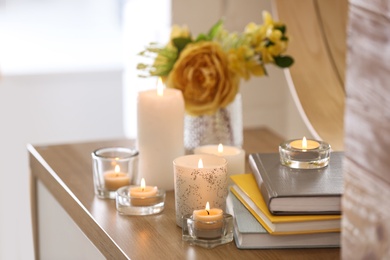 Beautiful burning candles, books and flowers on table at home