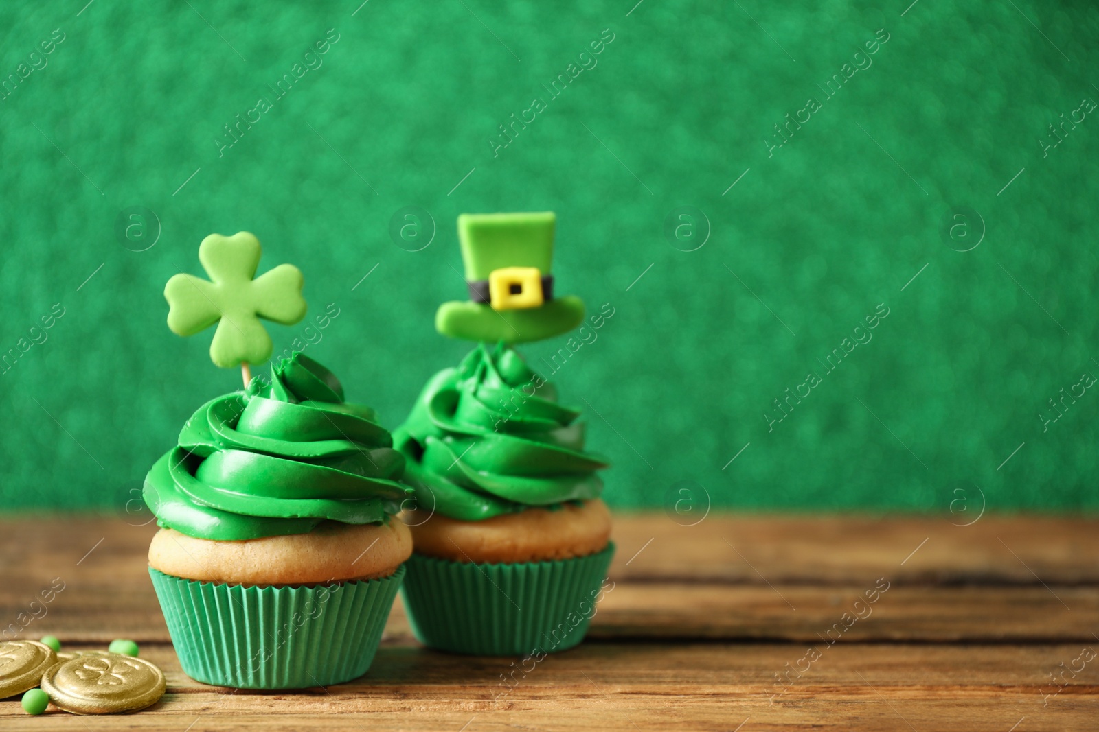 Photo of Decorated cupcakes and coins on wooden table, space for text. St. Patrick's Day celebration