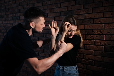 Photo of Man abusing scared woman near brick wall. Domestic violence