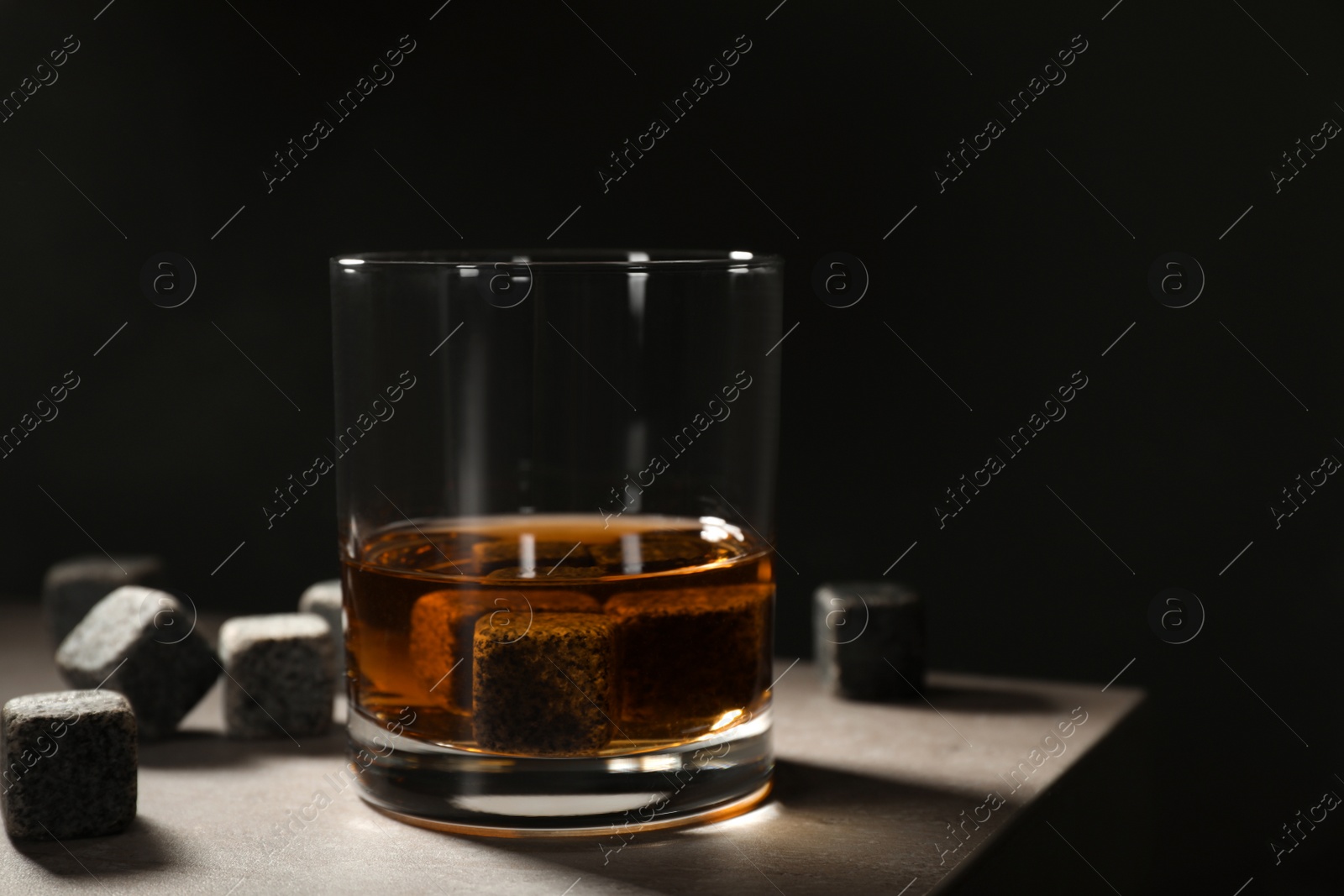 Photo of Golden whiskey in glass with cooling stones on table. Space for text