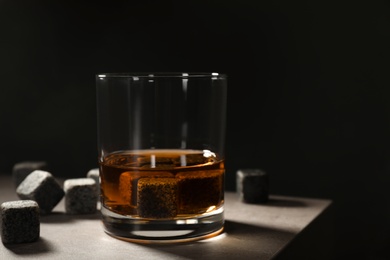 Golden whiskey in glass with cooling stones on table. Space for text