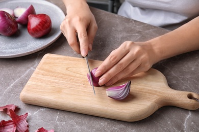 Photo of Woman cutting ripe red onion on table