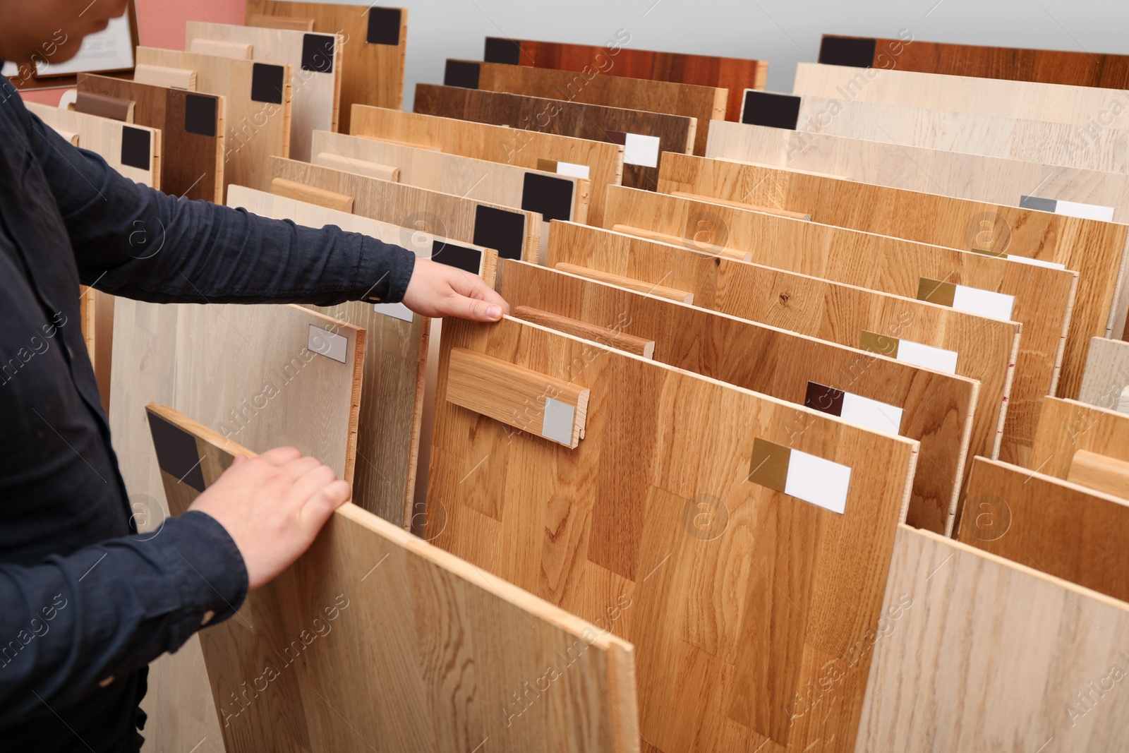 Photo of Man choosing wooden flooring among different samples in shop, closeup