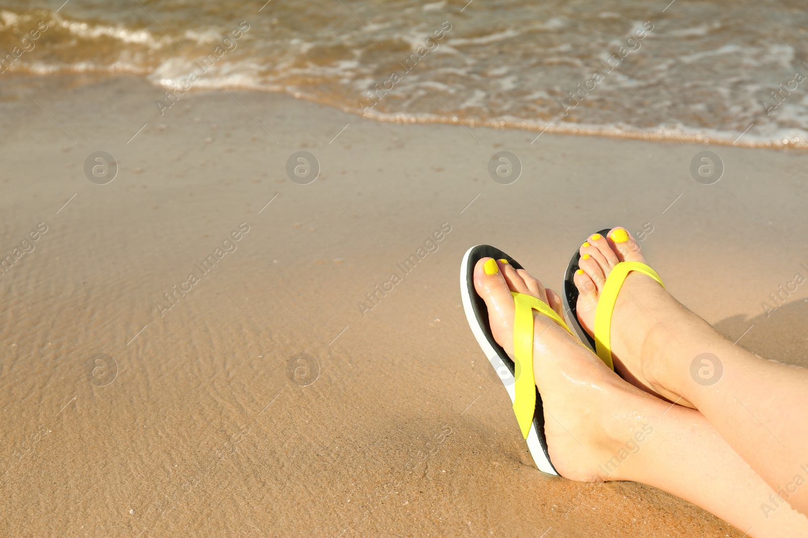 Photo of Closeup of woman with flip flops on sand near sea, space for text. Beach accessories