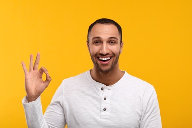 Photo of Smiling man with healthy clean teeth showing ok gesture on orange background