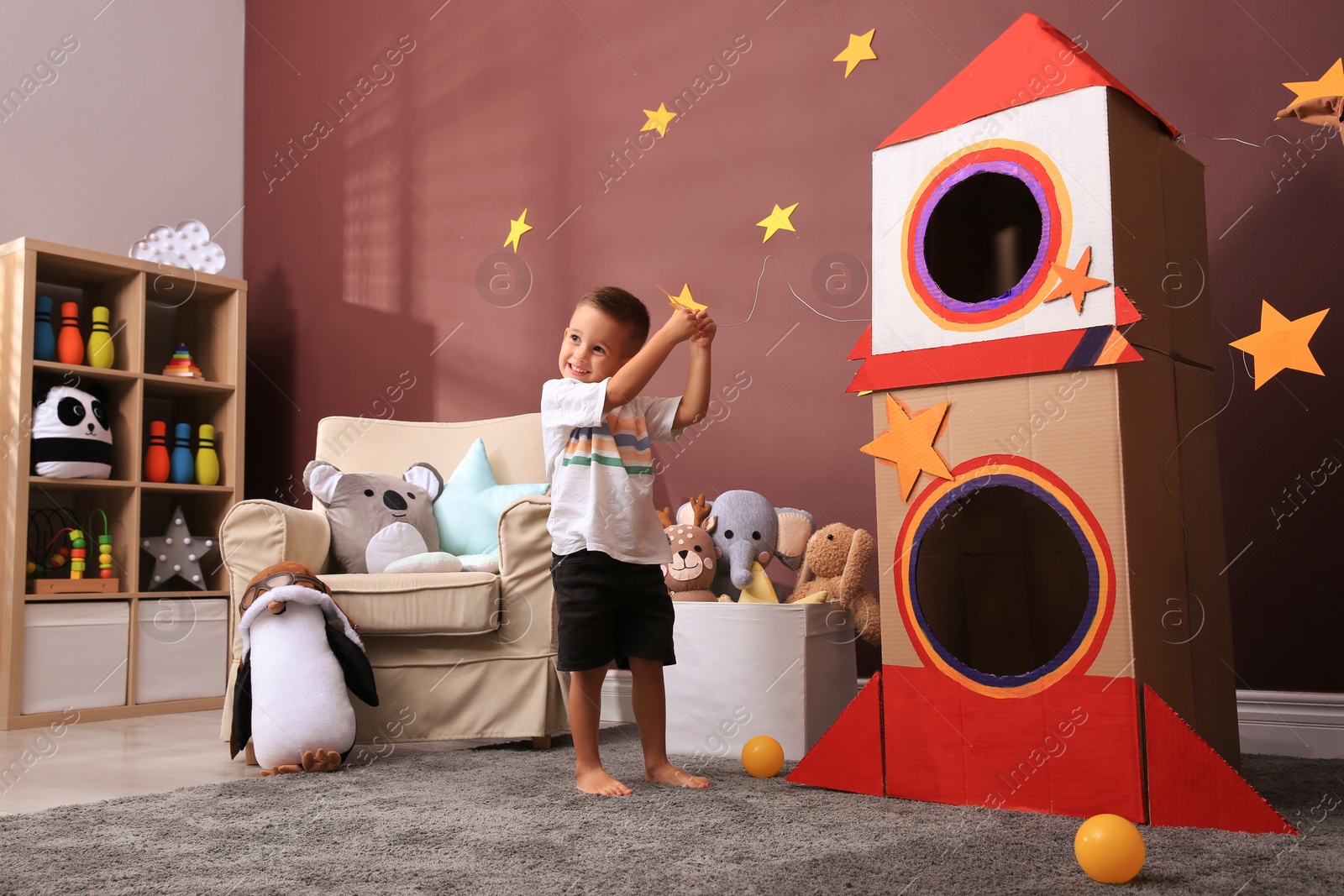 Photo of Cute little boy playing on floor near cardboard rocket  at home. Child's room interior