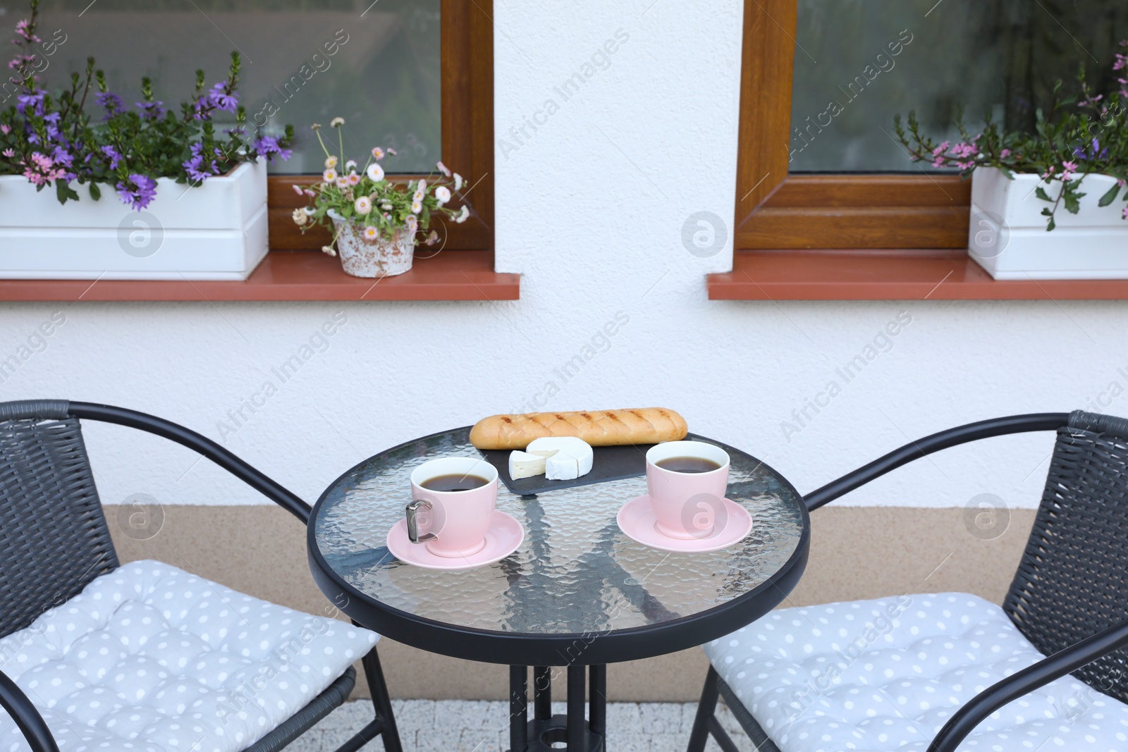 Photo of Cups of coffee, bread and cheese on glass table. Relaxing place at outdoor terrace