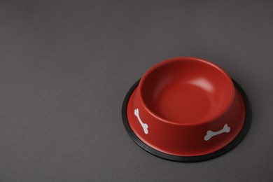 Photo of Empty red feeding bowl on dark grey background. Space for text