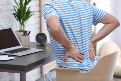 Young man suffering from back pain in office, closeup