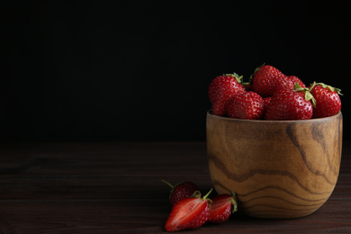 Photo of Delicious ripe strawberries in bowl on wooden table against black background. Space for text