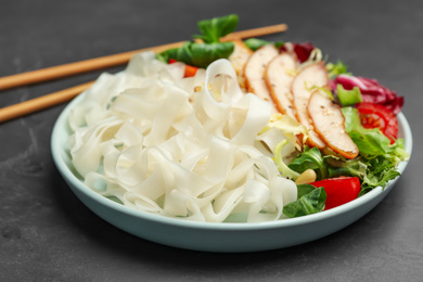 Photo of Tasty cooked rice noodles with chicken and vegetables on black table