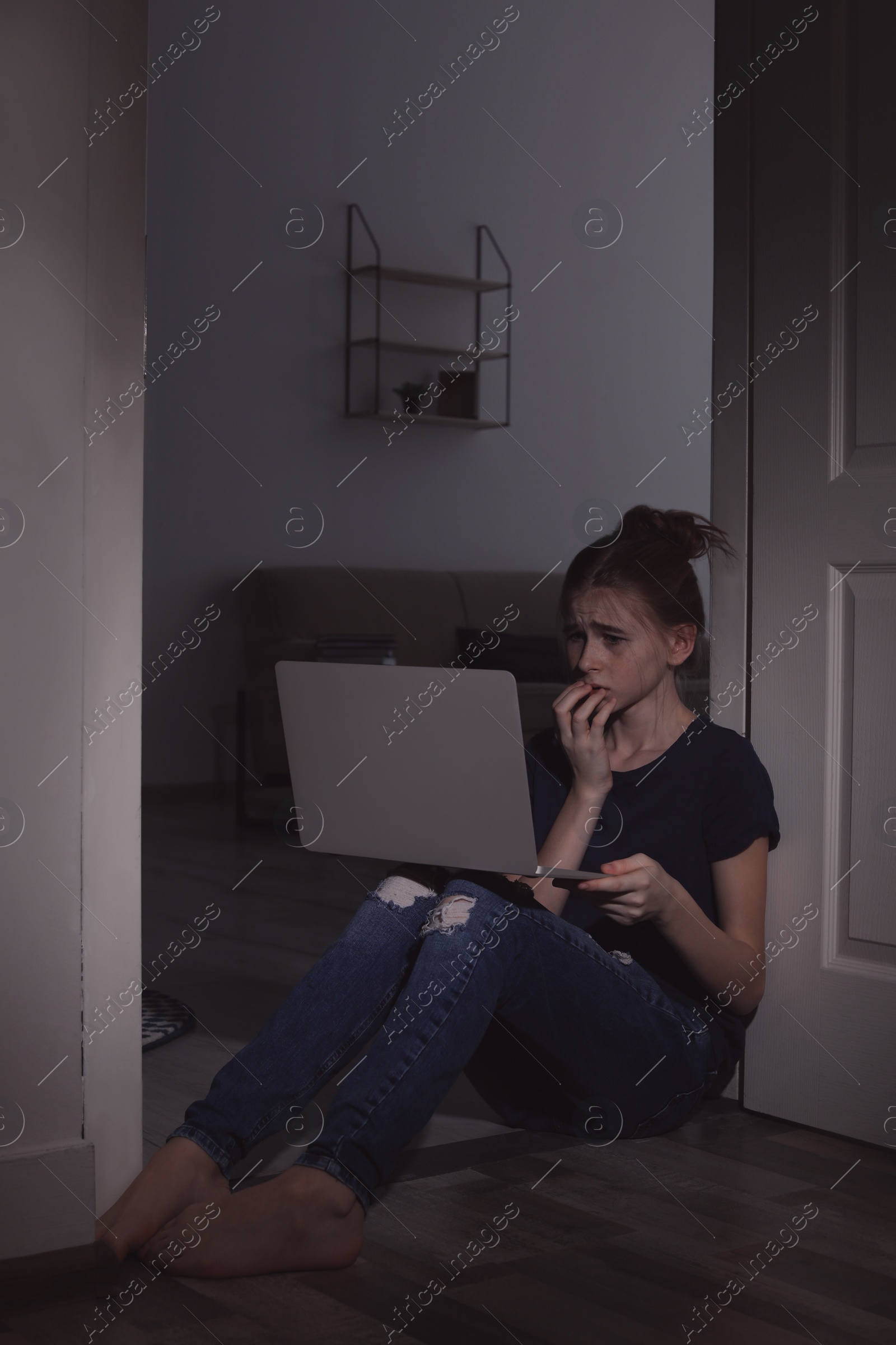 Photo of Frightened teenage girl with laptop on floor in dark room. Danger of internet